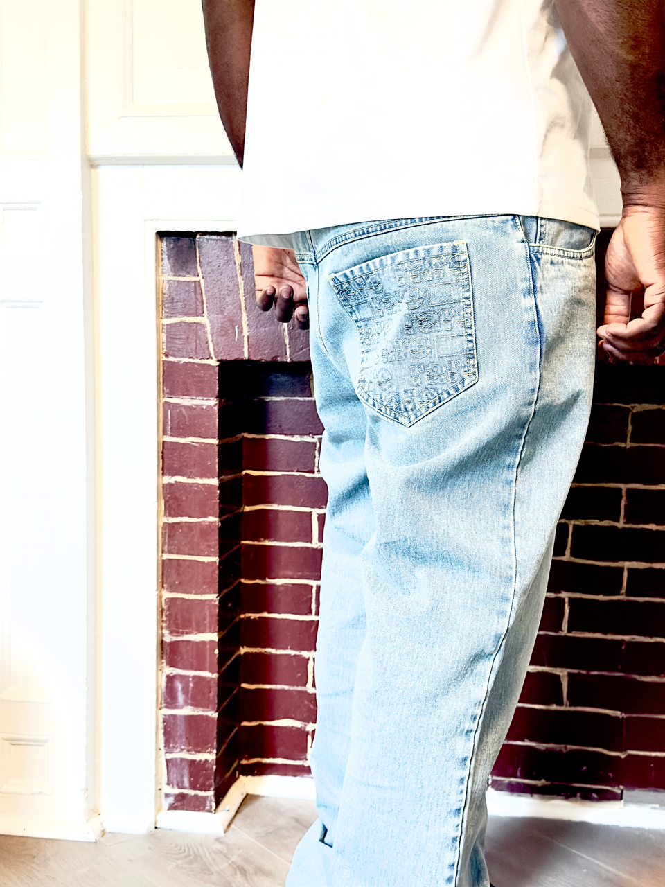 Person wearing light blue jeans standing in front of a brick wall.
